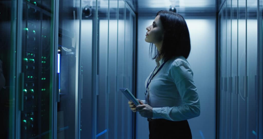 Female analyst holding a tablet reviews servers in a data center.