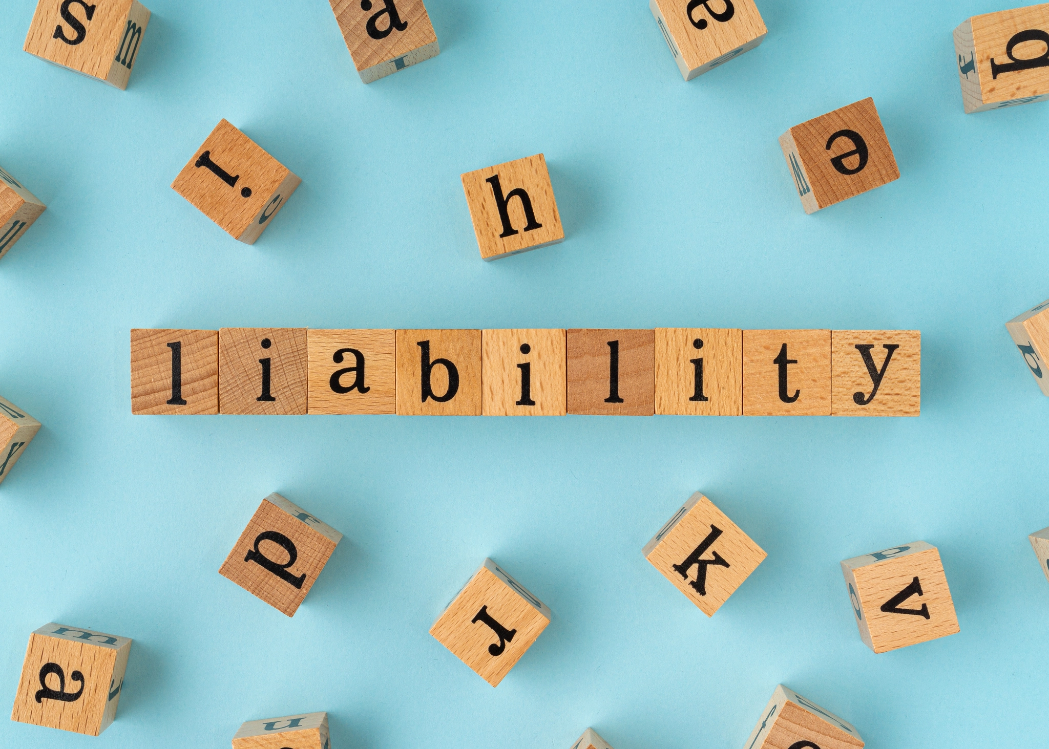 "Liability" is spelled out using Scrabble tiles against a light blue backdrop.