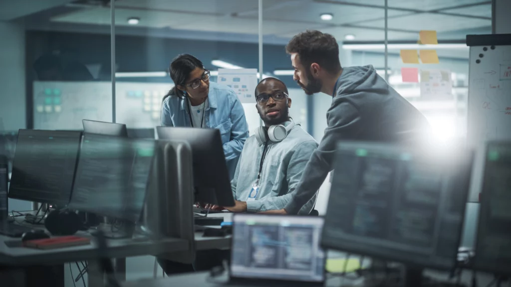 Three cybersecurity specialists talk in front of a bank of computers.