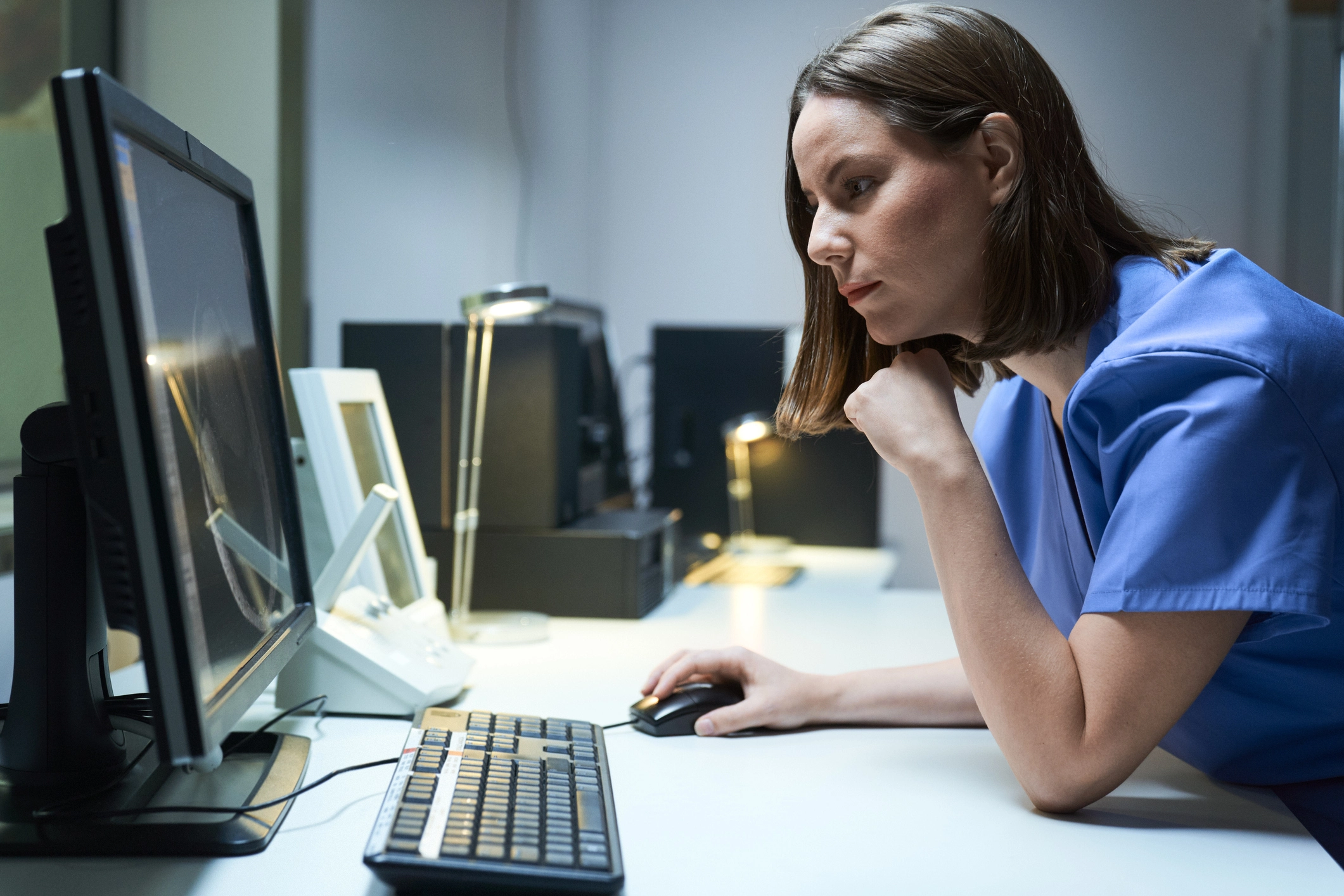 A healthcare worker uses a desktop computer to review patient care data.