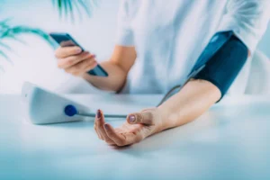 A patient checks health vitals on their smartphone while using a blood pressure cuff.