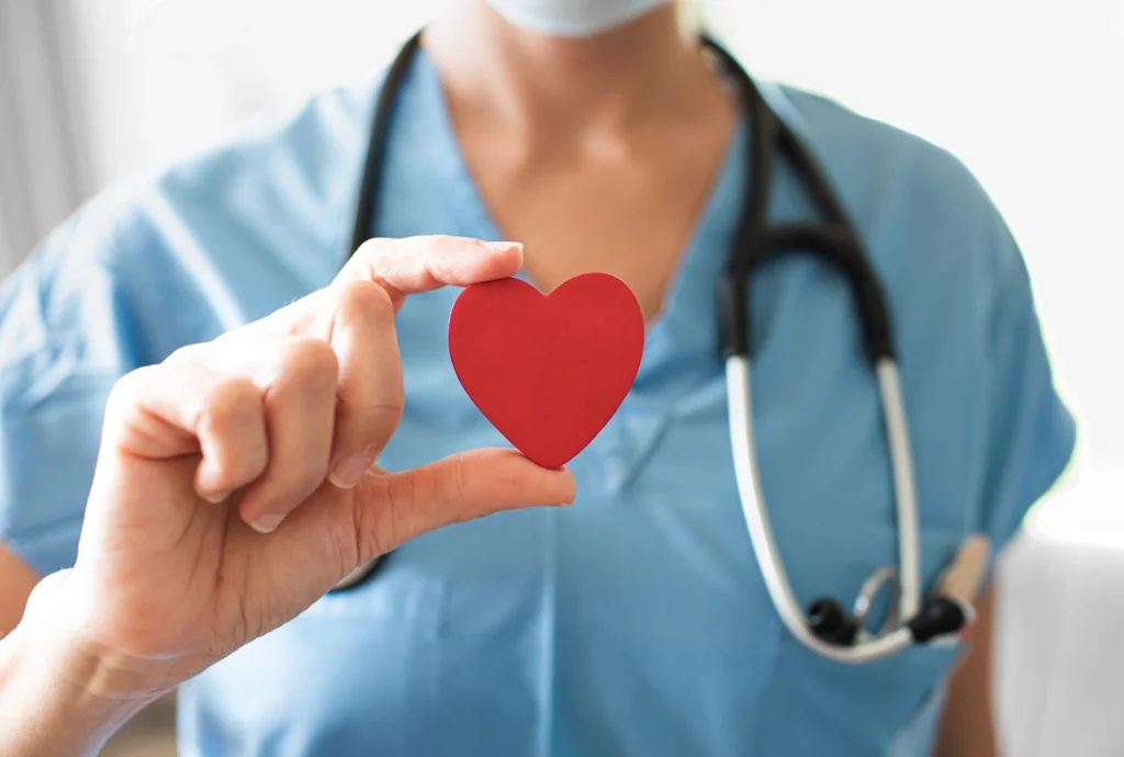 A nurse holds a red heart to represent a remote patient monitoring solution for chronic care.