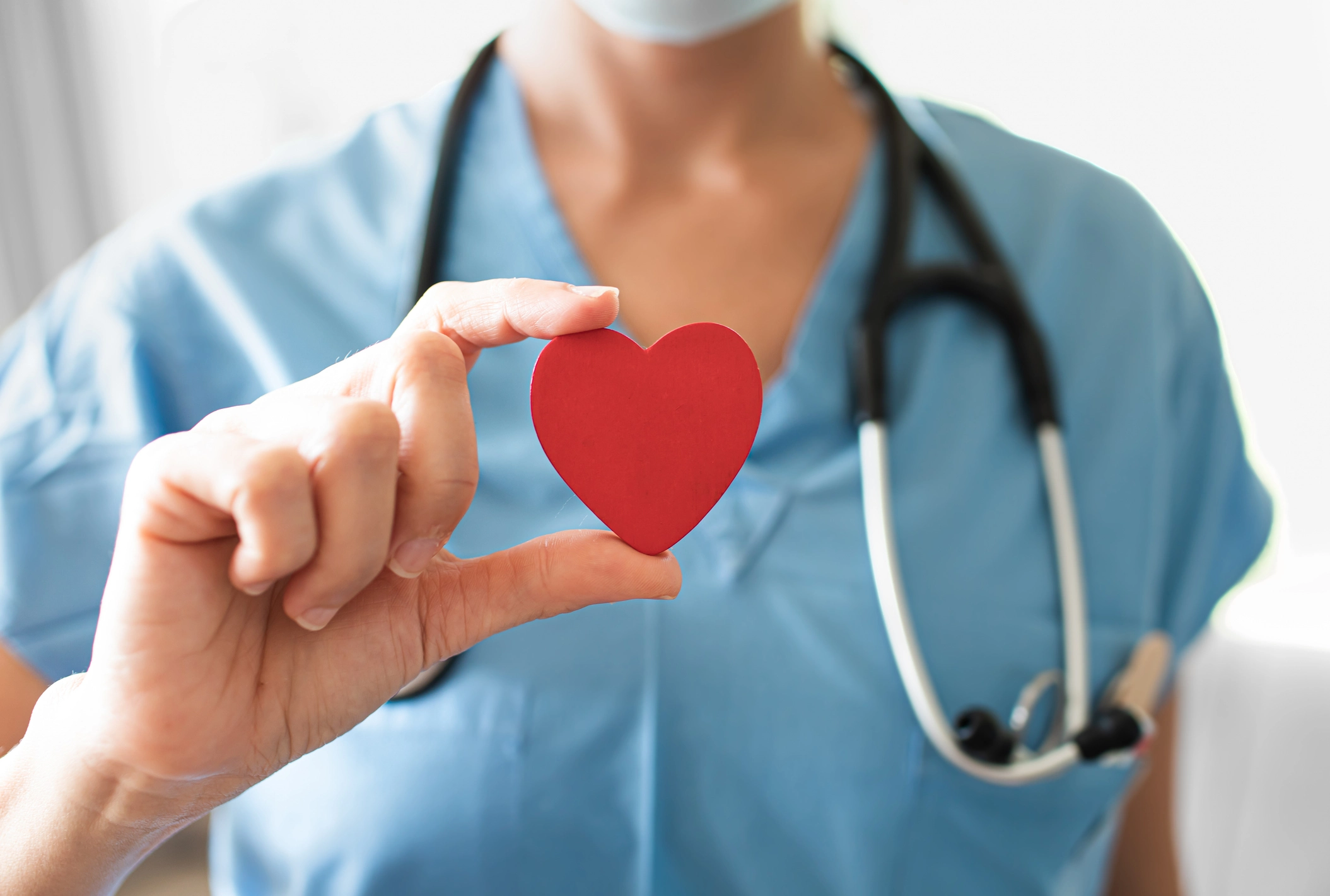 A nurse holds a red heart to represent a remote patient monitoring solution for chronic care.